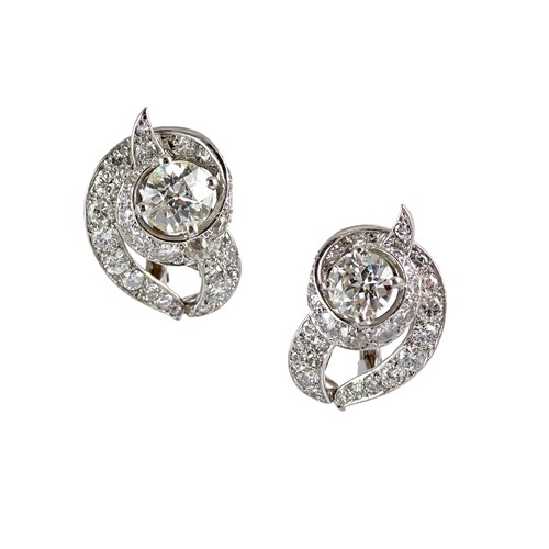 Pair of diamond scroll earrings by Cartier, London, with a looping ribbon around a principal old round brilliant cut diamond,
